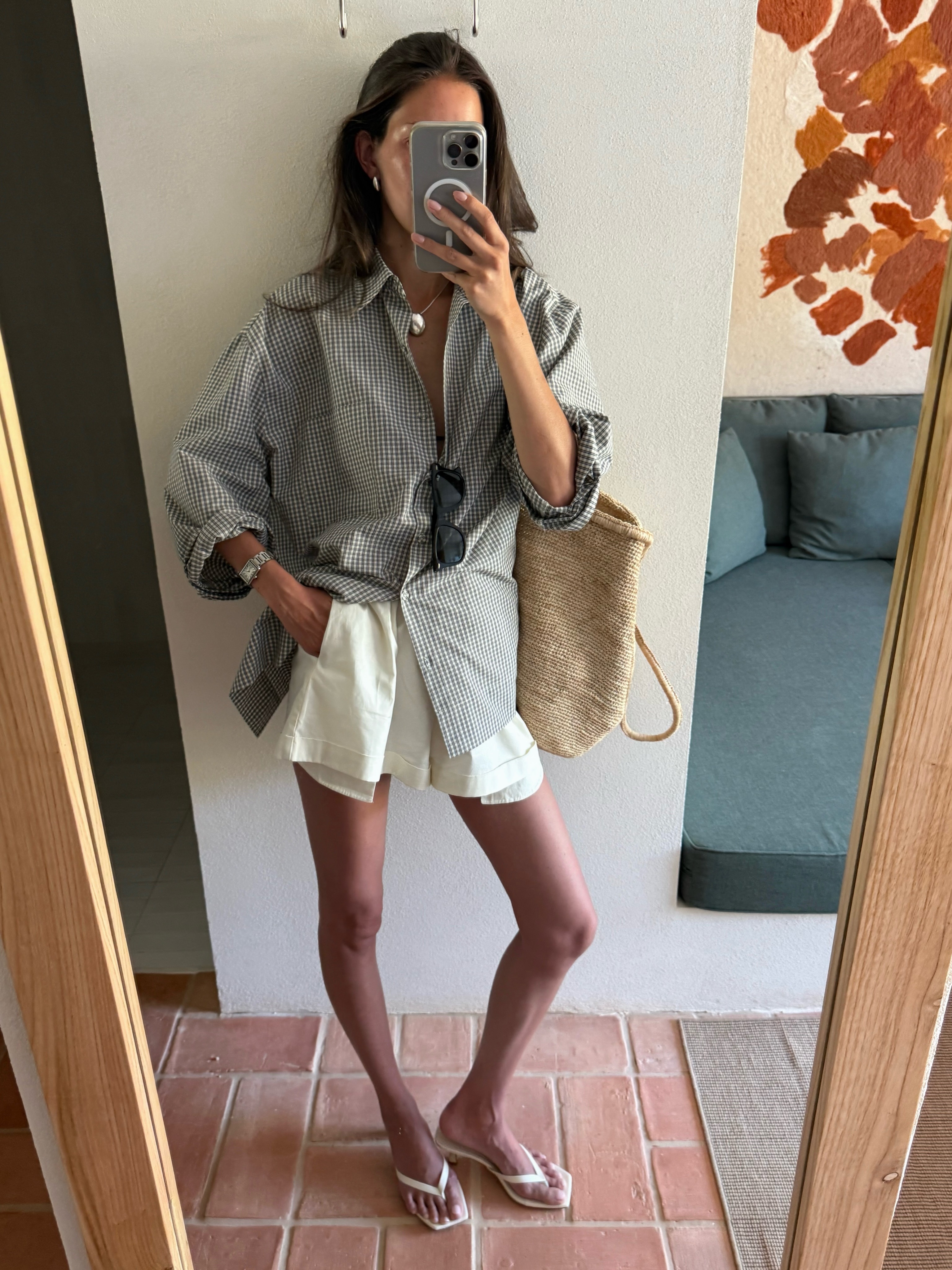 Fashion person Fakerstrom is wearing the June Outfit Ideas 2026 look. She is wearing a gingham shirt, white mini shirt and white minimalist sandals. In the recent image she ends up carrying a large raffia bag.