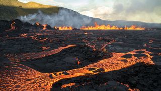 Lava trickles over volcanic rocks and catches fire.