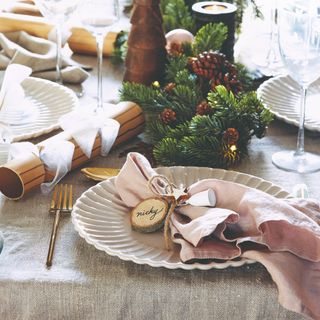 A dining table set for a Christmas dinner with a pink linen napkin pinched and pulled and tied with a twine