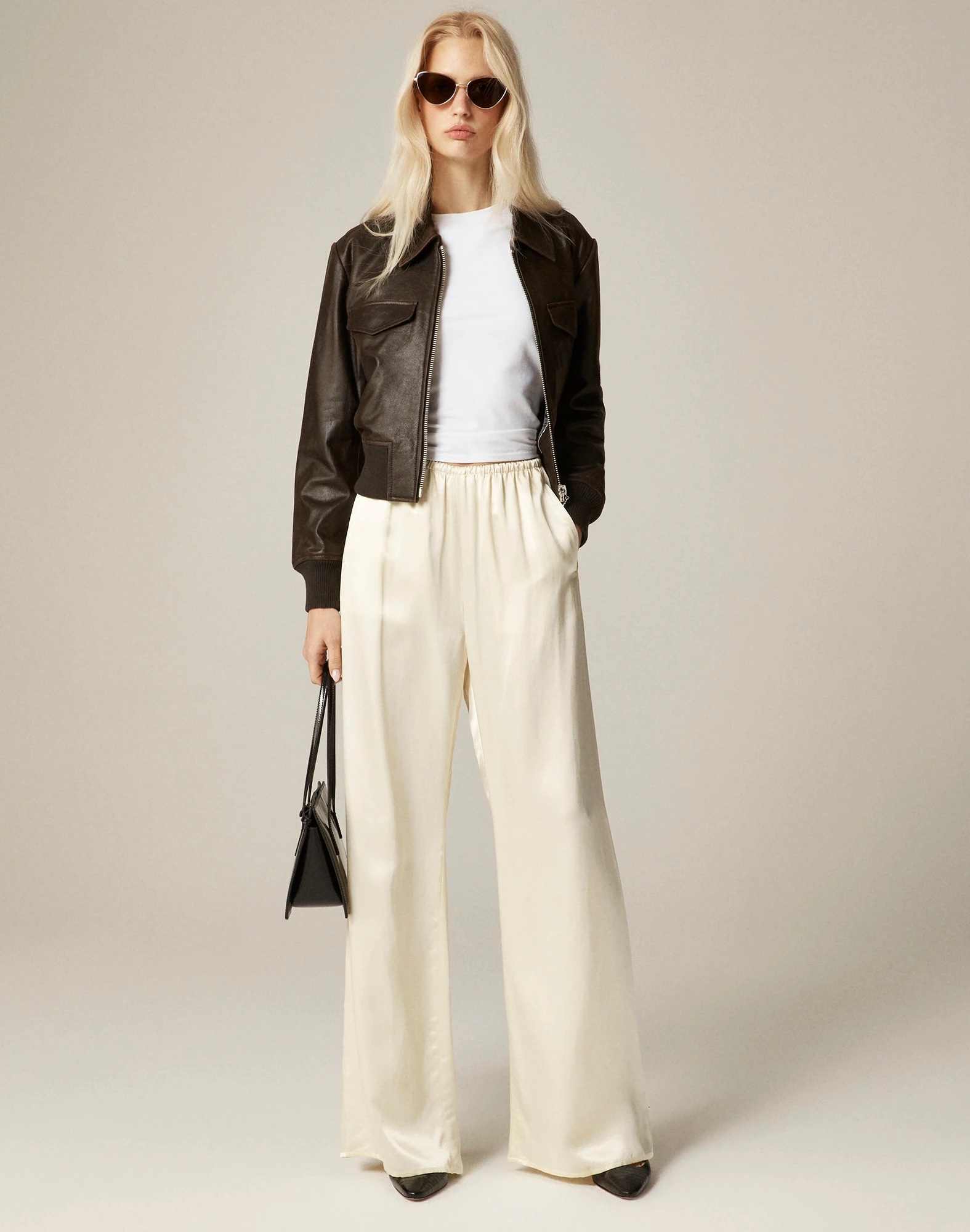 J.Crew fall 2025 collection outfit idea with a brown leather jacket, metal-rim sunglasses, a white t-shirt, a cream charmeuse satin drawstring pants, and black shoes