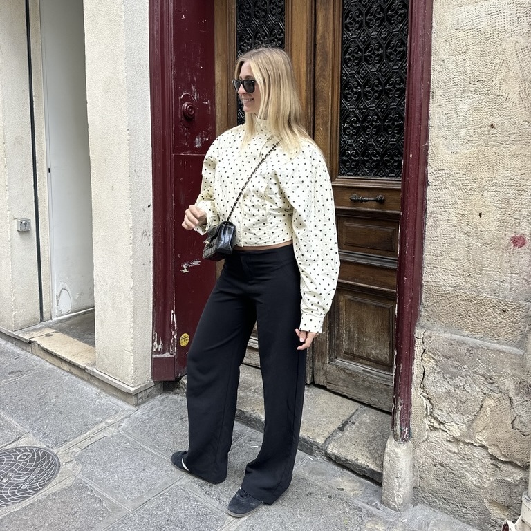 bailey burke wearing a polka dot jacket with black trousers and black adidas and a black chanel crossbody and sunglasses