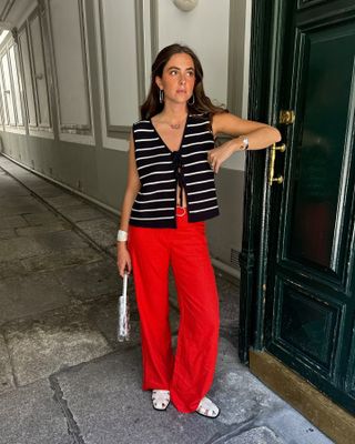 Alex is wearing red pants, white fisherman flats, a silver handbag, and a striped knit top.