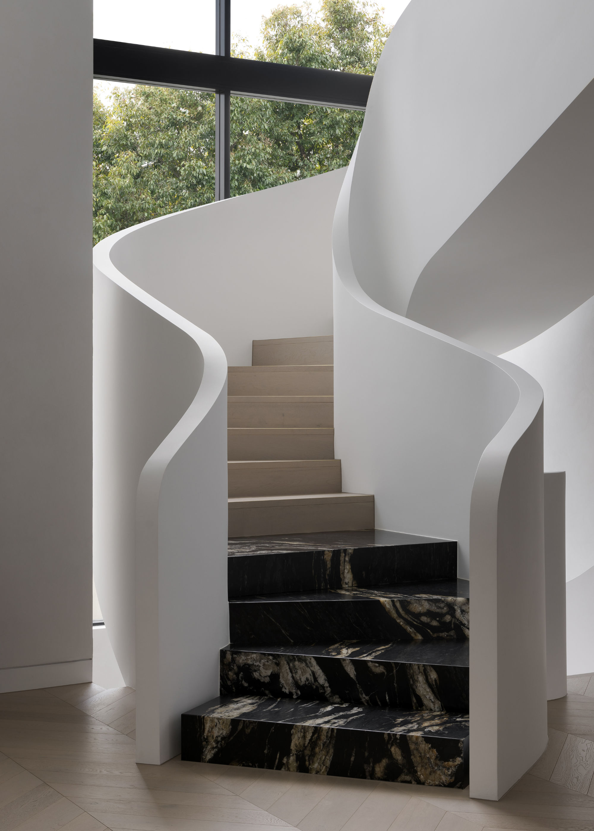 a white curving staircase in a glass room with four marble steps at the bottom of a wooden staircase