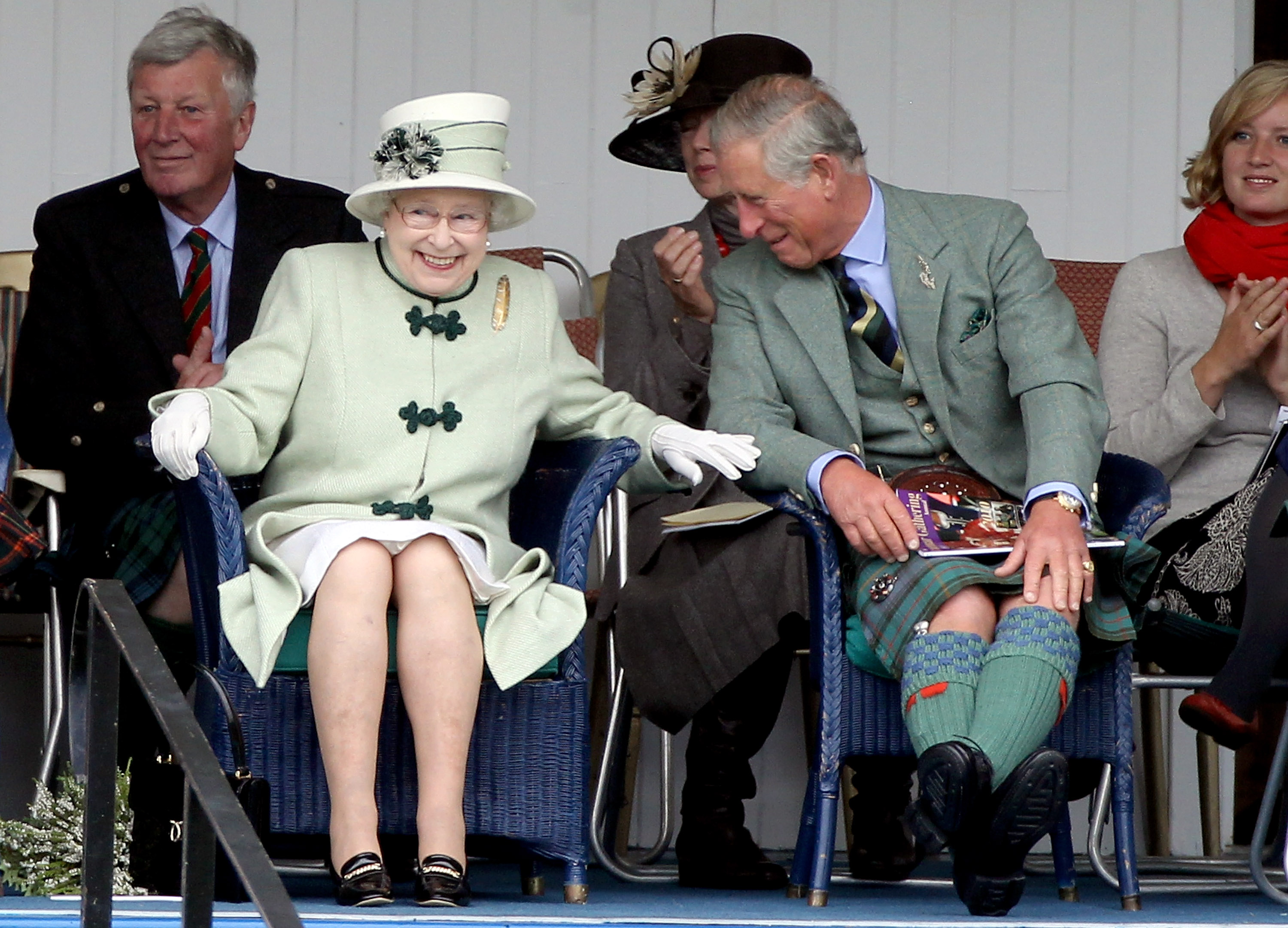 Queen Elizabeth sitting in a chair and touching King Charles's arm, who is laughing