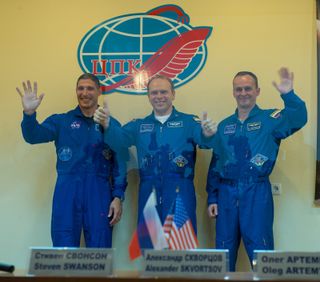 Expedition 37 NASA Flight Engineer Michael Hopkins, far left, Soyuz Commander Oleg Kotov and Russian Flight Engineer Sergey Ryazanskiy, far right, wave and give the thumbs up following a press conference held at the Cosmonaut Hotel, on Tuesday, Sept. 24, 2013, in Baikonur, Kazakhstan.