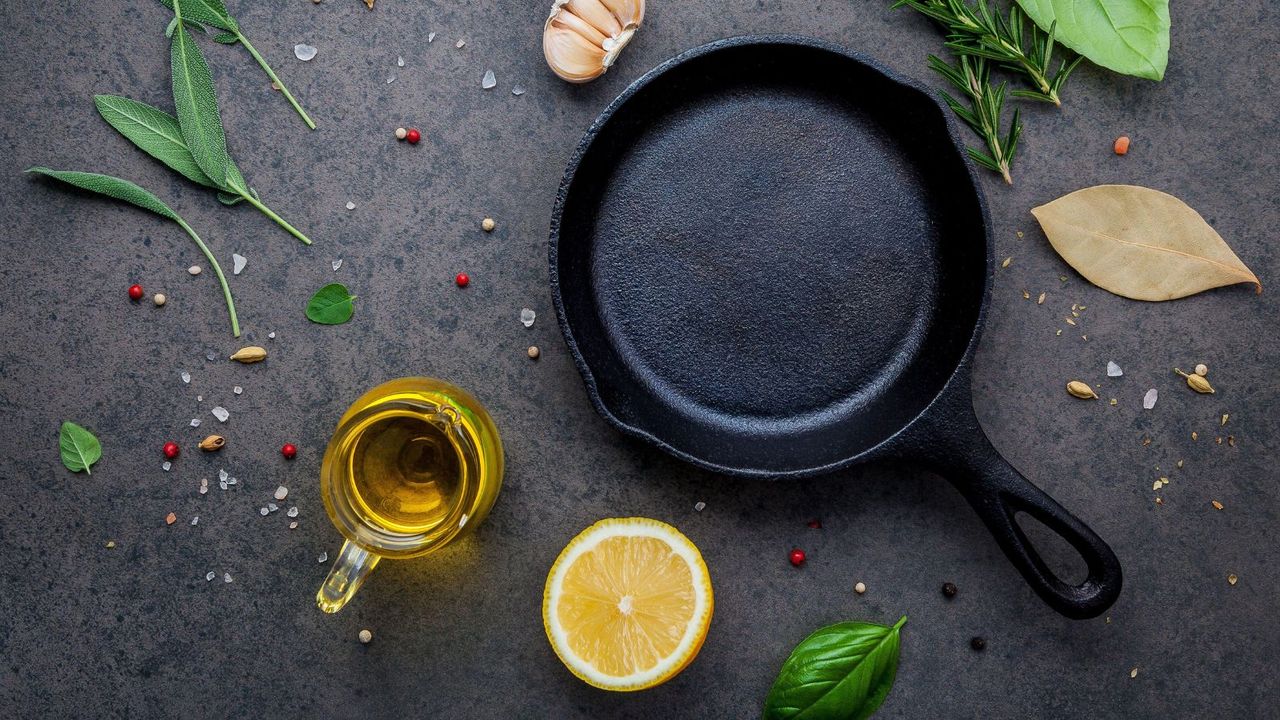 A cast iron pan besides a glass jug of oil and a lemon