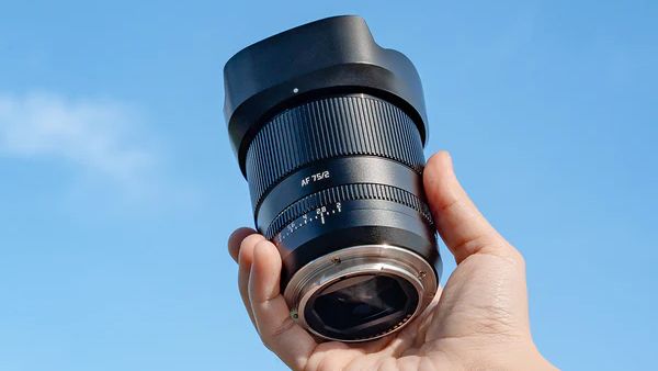 The TTArtisan 75mm f/2 lens held in a hand against a blue sky