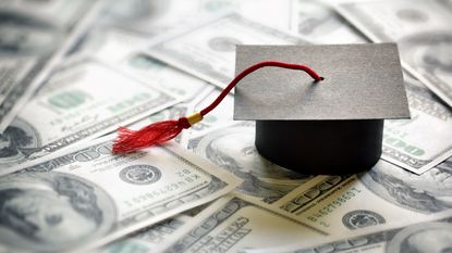 A graduation cap on a pile of hundred dollar bills. 