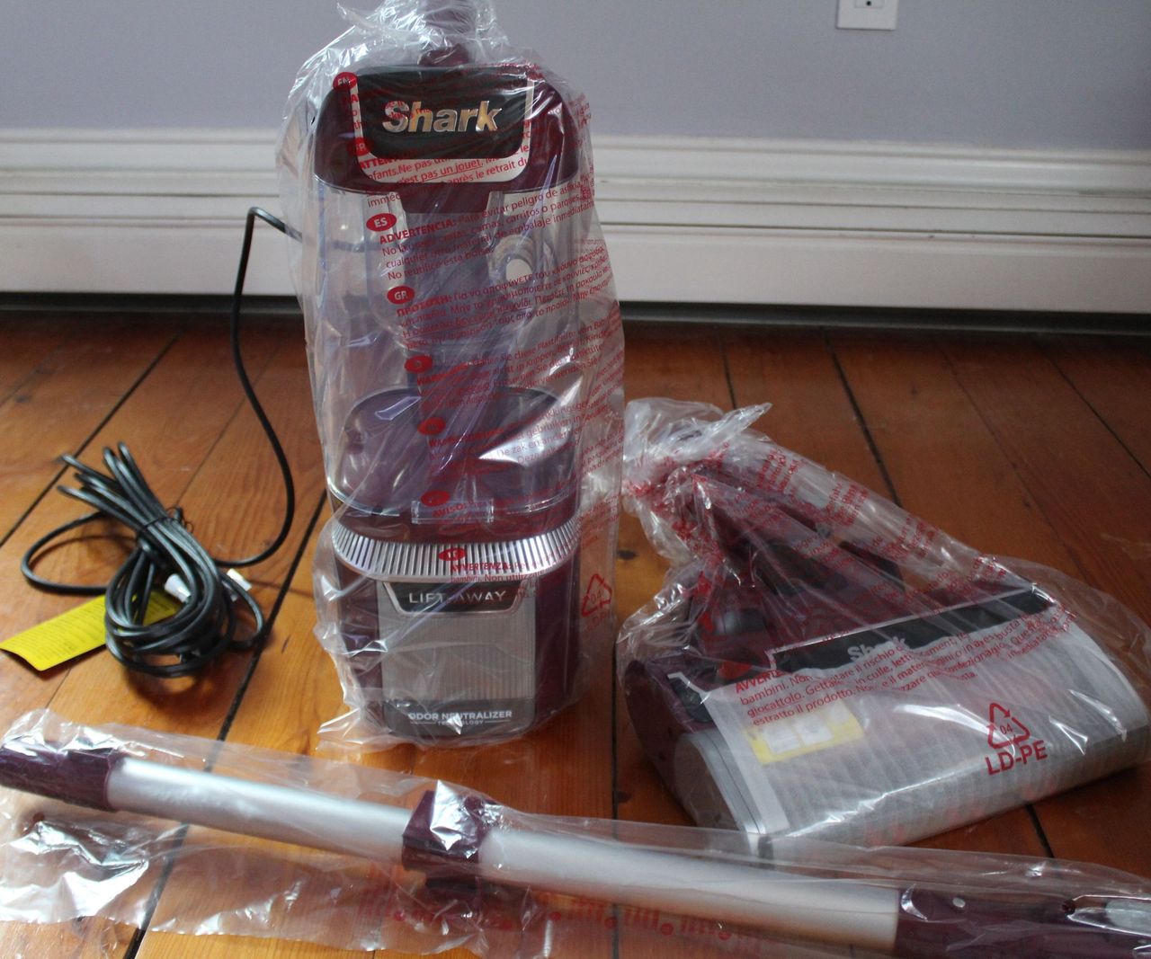 The parts and attachments of the Shark Rotator, in sealed bags, laid out on a wooden floor