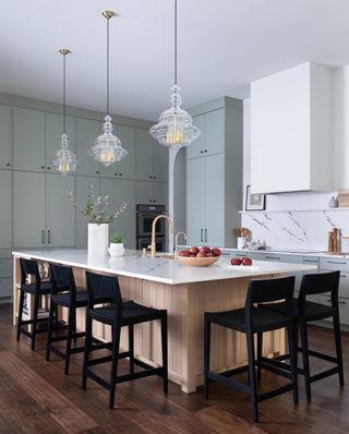 white kitchen with sage green cabinets, wood island with marble worktop and black stools