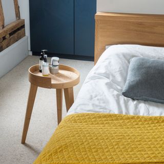 Round side table next to bed in light coloured room with yellow throw