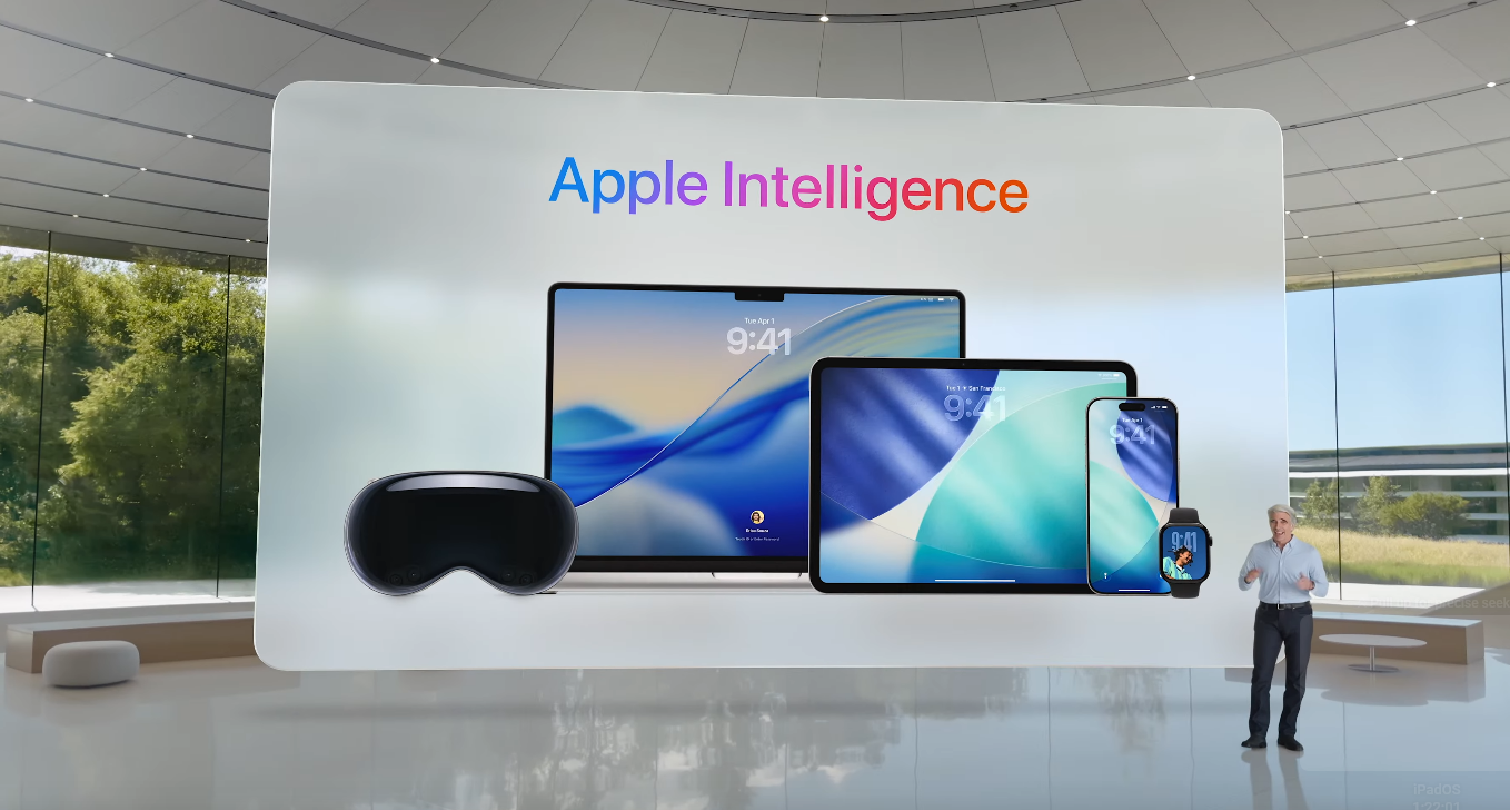 A presenter stands on stage in front of a large screen displaying the words “Apple Intelligence” in a colorful gradient. 
