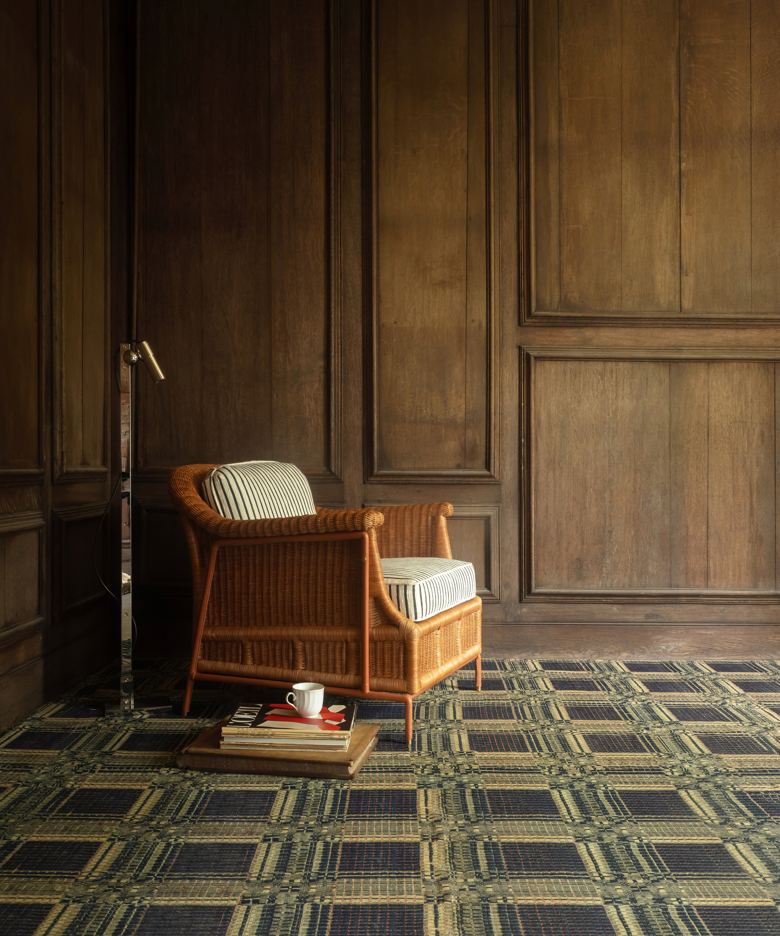 rattan reading chair in the corner of a wood panelled room on a graphic rug