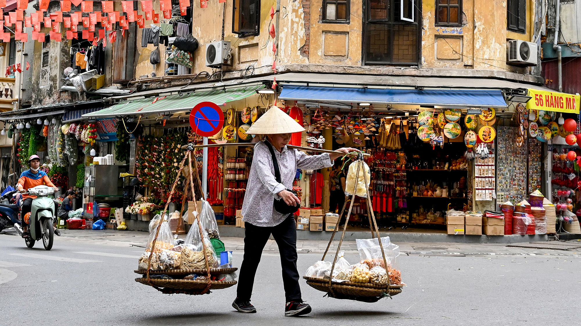 A street vendor walks down a street carrying food for sale in Hanoi, Vietnam