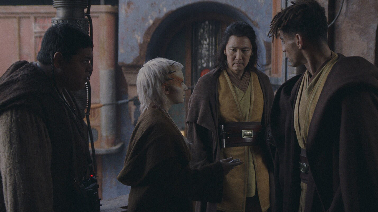 people in brown robes stand around in desert-looking dwellings