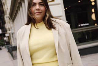 Woman standing on New York City street wearing beige blazer, yellow vest, and yellow maxi skirt.