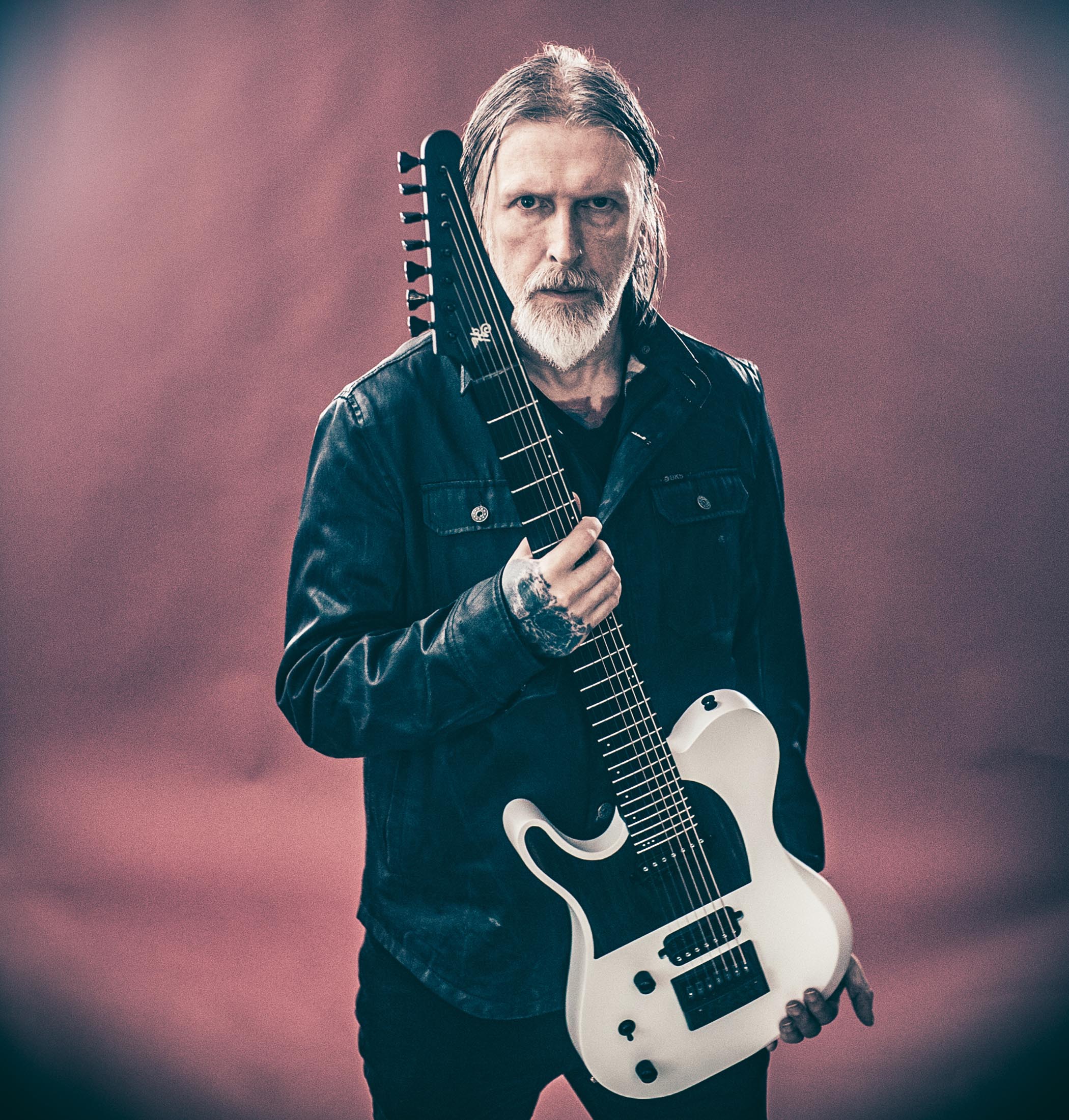 Greg Mackintosh of Paradise Lost poses in front of a pin-purple background with a white 7-string T-style from German brand Hapas.