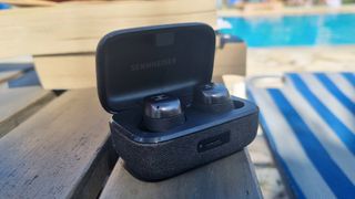 The Sennheiser Momentum True Wireless 4 earbuds in their case next to a pool