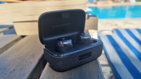 The Sennheiser Momentum True Wireless 4 earbuds in their case next to a pool