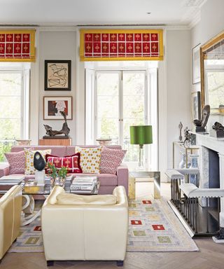 Colorful white living room with red and yellow patterned blinds, patterned rug, fireplace, pink sofa, cream leather lounge chair