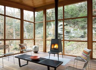 screened in porch looking onto a forest, with a woodburner