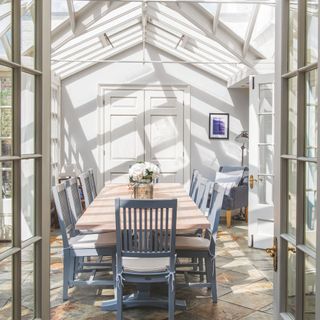 Dining table and chairs in a light-filled conservatory with double doors at both ends