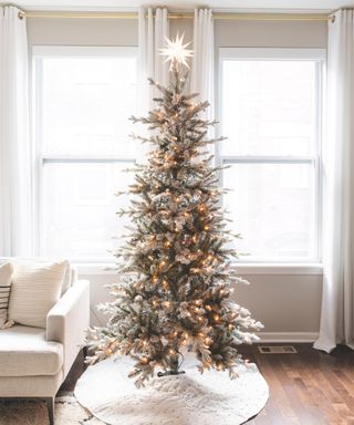 A flocked Christmas tree in front of a large window