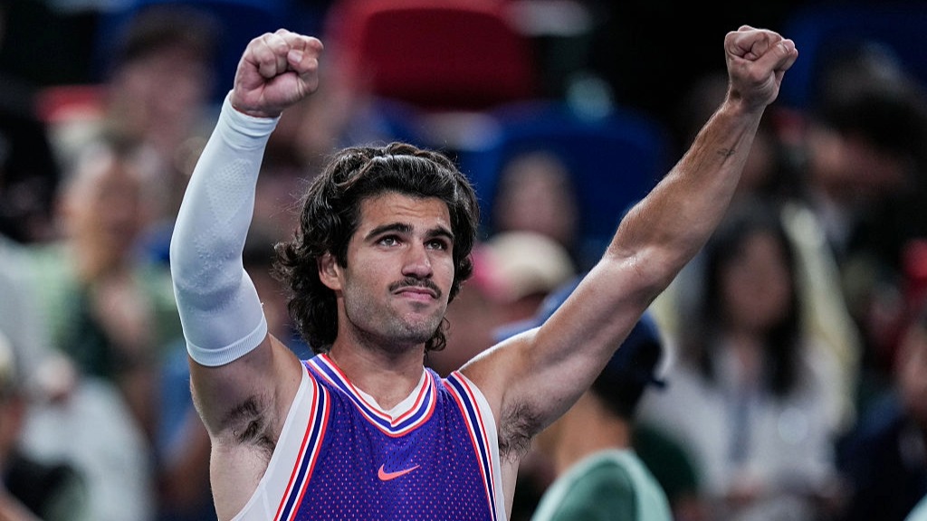 Carlos Alcaraz, sporting a new moustache, raises his arms in celebration at winning a match at the Shanghai Masters 2026.