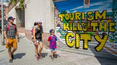 A visiting family walks past anti-tourism graffiti against tourism in Barcelona