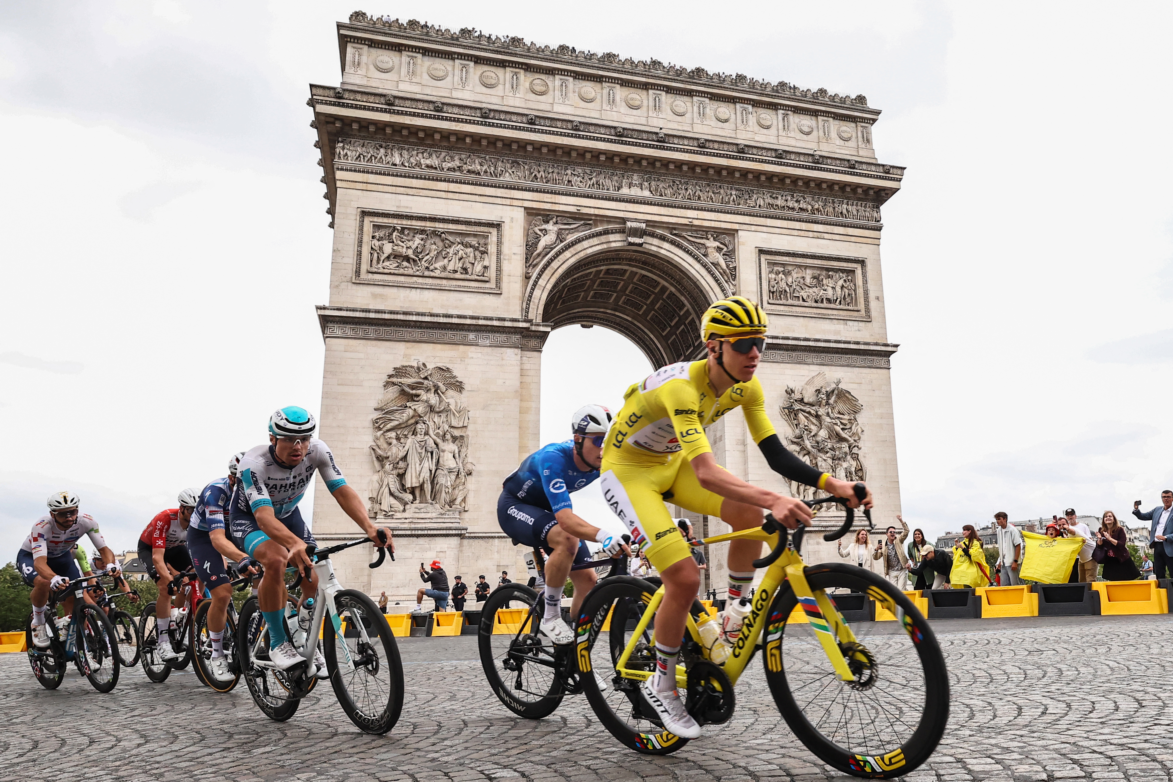 Guest and UAE Team Emirates - XRG team's Slovenian rider Tadej Pogacar wearing the overall leader's yellow jersey cycles with the pack of riders (peloton) past the Arc de Triomphe on Place Charles de Gaulle during the 21st and final stage of the 112th edition of the Tour de France cycling race, 132.3 km between Mantes-la-Ville and Paris' Champs-Elysees Avenue, on July 27, 2025. (Photo by Anne-Christine POUJOULAT / AFP)