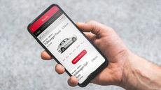 An outstretched hand holds a smartphone with the Avis app on screen