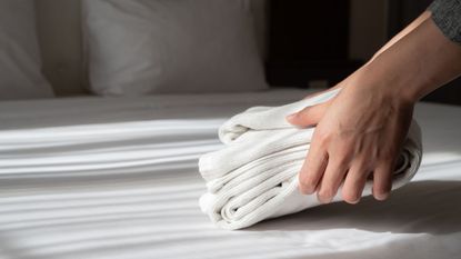 Someone placing some folded up linens on a white bed