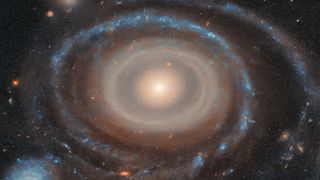 A swirling galaxy like a bullseye with blue and tan and orange gases around a central bright point.