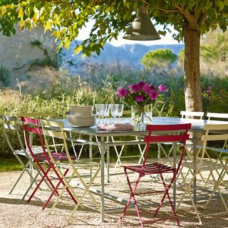 dining table and chairs in open garden with plants and tree