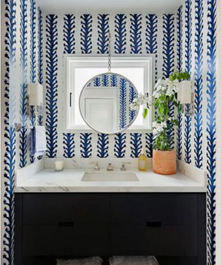 A powder room with blue and white wallpaper, a marble vanity unit and a round mirror