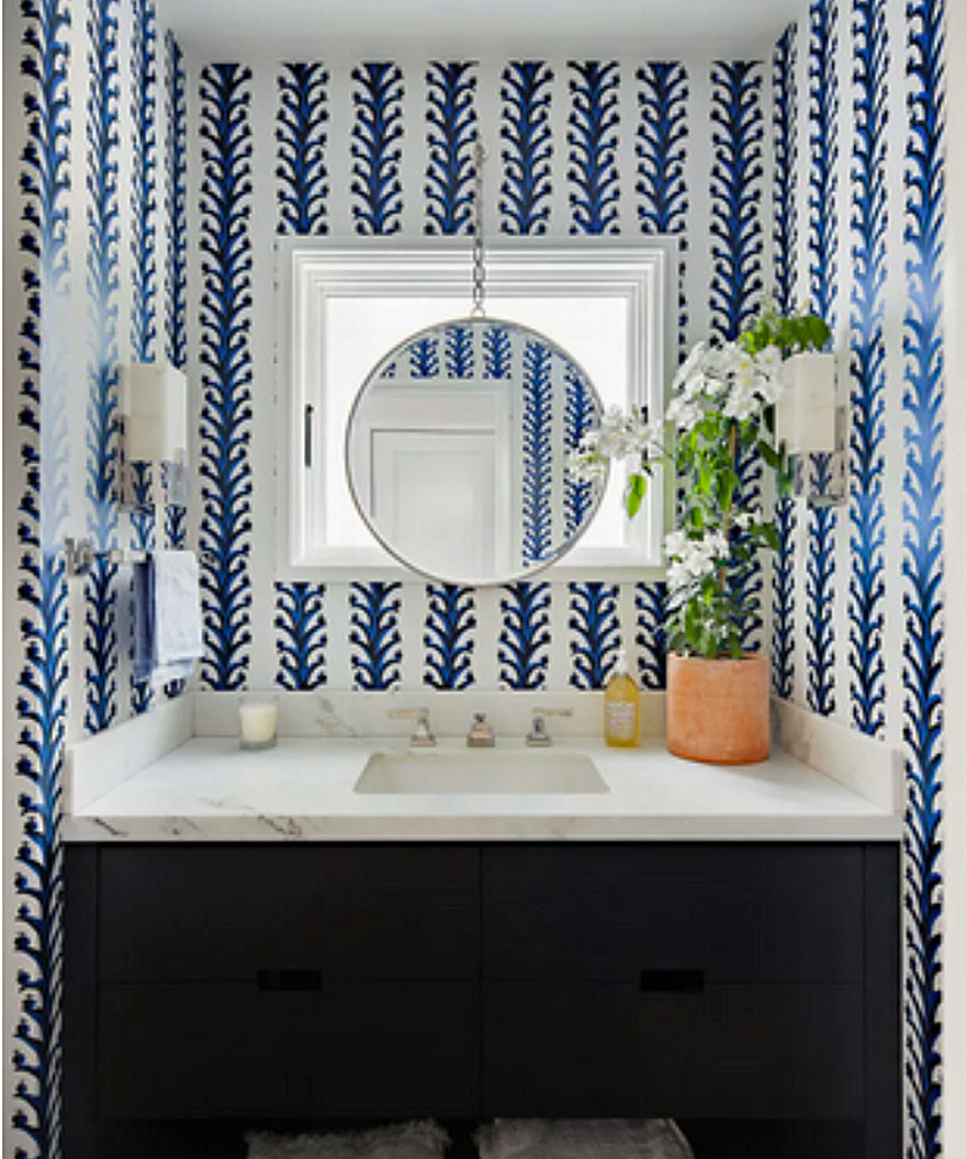 A powder room with blue and white wallpaper, a marble vanity unit and a round mirror