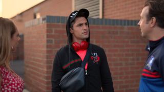 Phil Dunster as Jamie wearing a hat that says "icon" and bright red headphones.