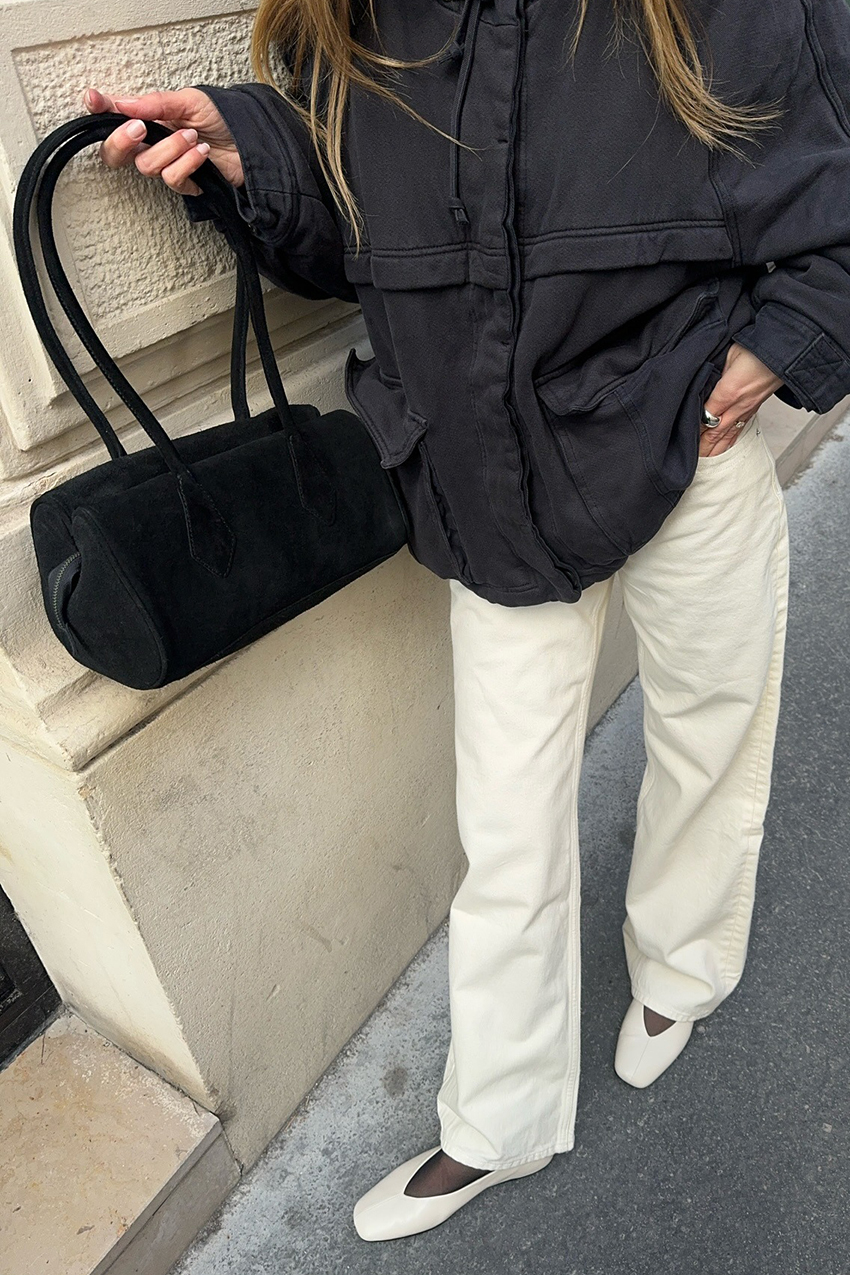 a woman wearing a black jacket, black bag, white jeans, and white shoes