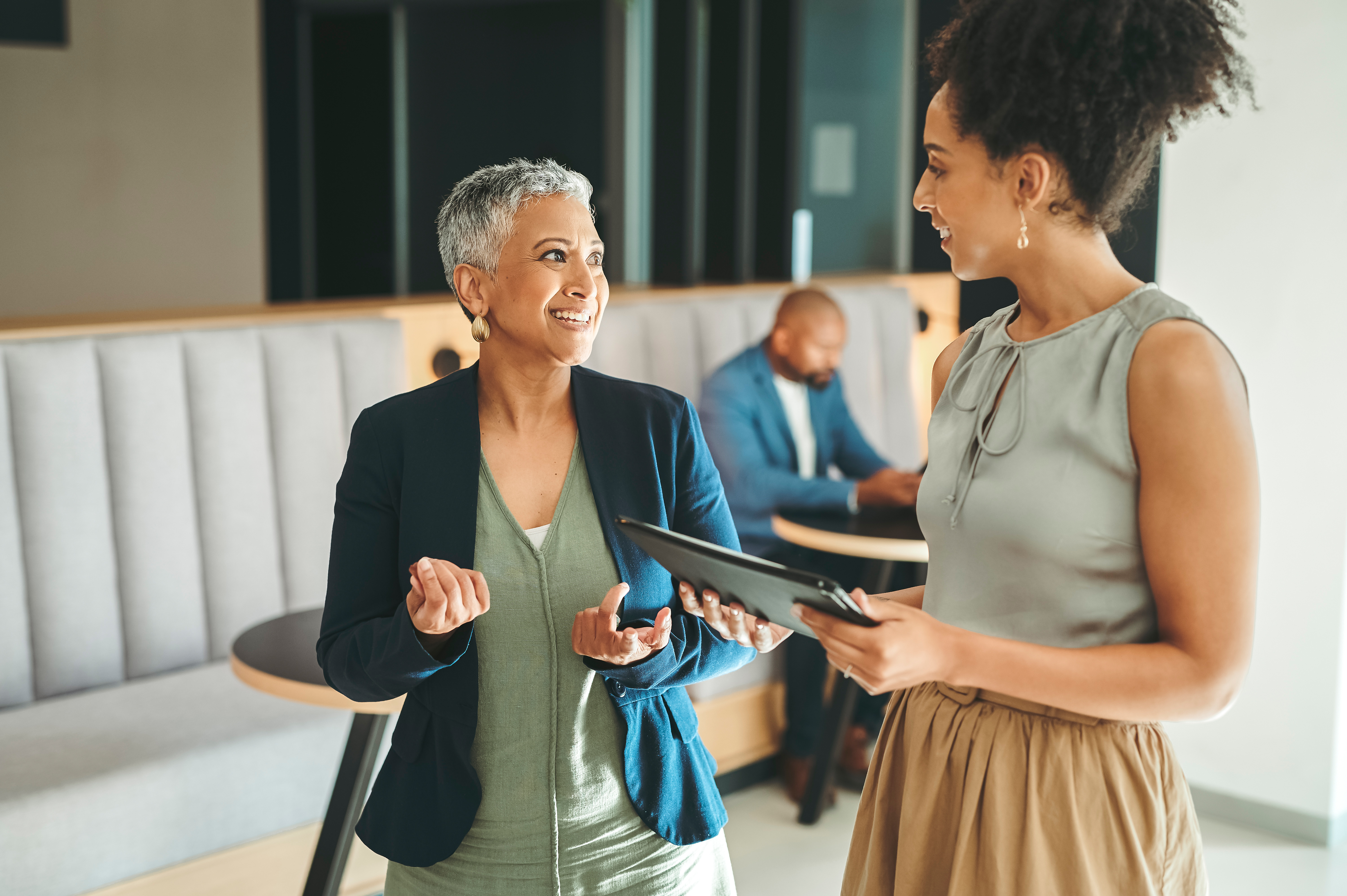 Older and younger employee stand having discussion in workplace.