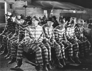 a group of inmates wearing striped prison clothes sit chained together in the movie I Am a Fugitive from a Chain Gang