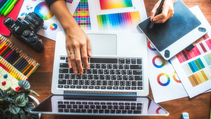 A designer using a laptop and tablet, surrounded by color palettes