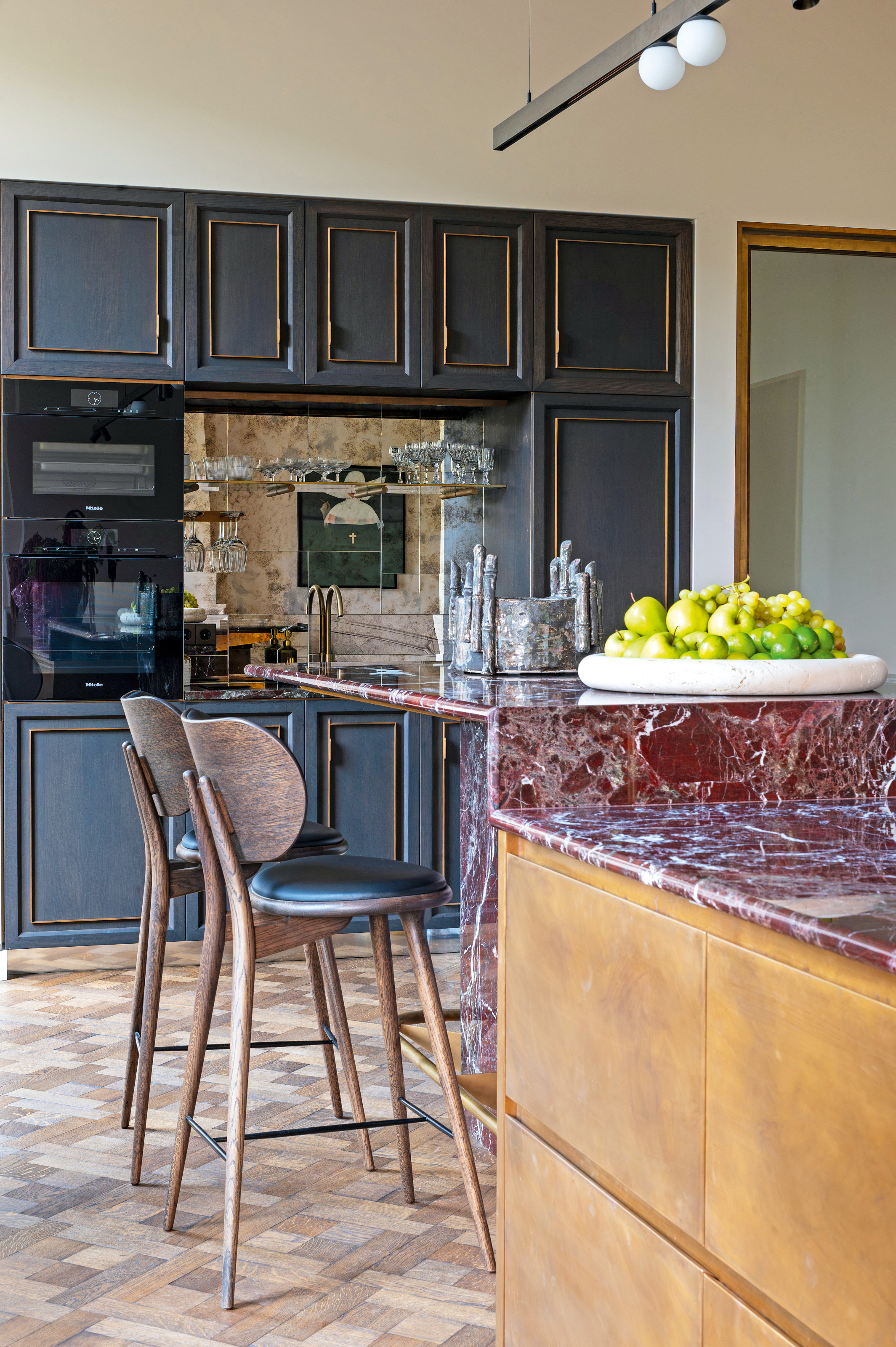 Kitchen with two-tier island with red marble countertop, bronze cabinets, blue wall units and wood and black leather bar stools
