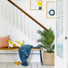 White hallway with bench, staircase, plant and artwork
