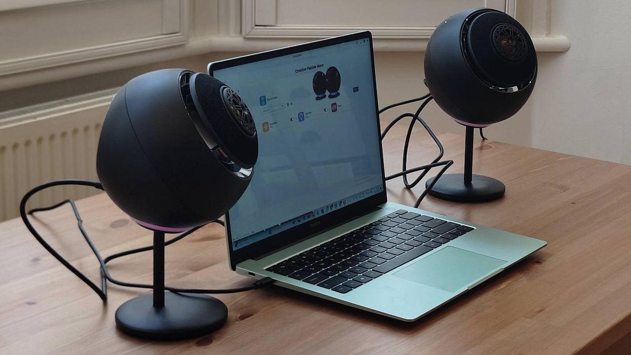The Creative Pebble Nova on a brown table, connected to a green laptop.