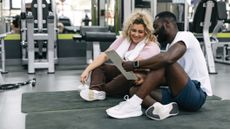 Man and woman sitting on exercise mats in gym looking at a clipboard