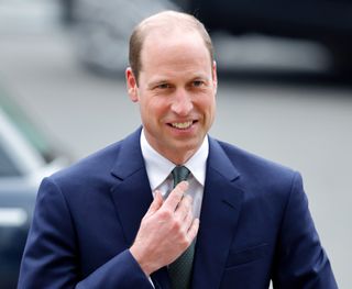 Prince William is clean shaven and wears a navy suit with a white shirt and blue tie