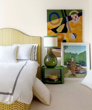 neutral bedroom with yellow upholstered bed and layered artwork