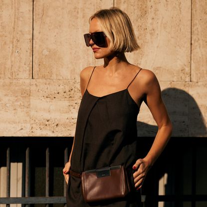woman with short blonde hair wearing sunglasses black tank top and brown fanny pack