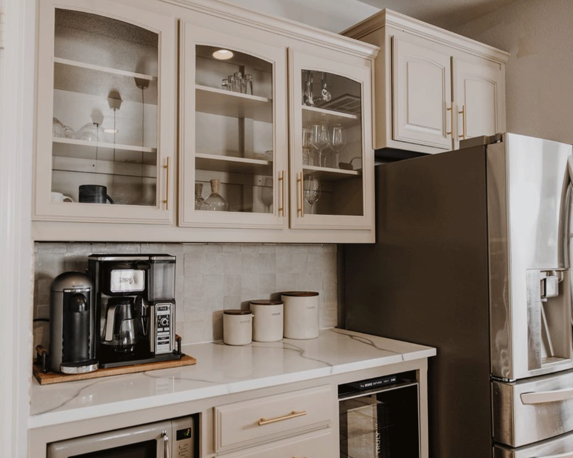 close-up view of a modern all-white kitchen, with a large coffee machine, pots for tea and coffee, cabinets with glass doors, and a large stainless steel fridge