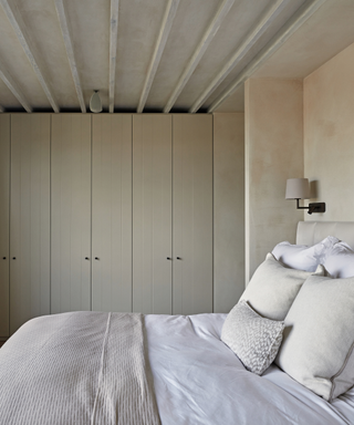 minimalist modern bedroom in muted natural colours with inbuilt wardrobe in background and bed in foreground